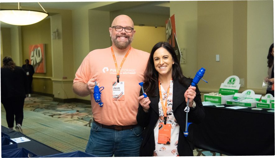 Two smiling attendees holding blue items at a conference or event